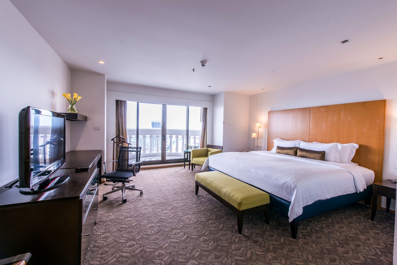Hotel suite with king size bed green stool and desk with chair
