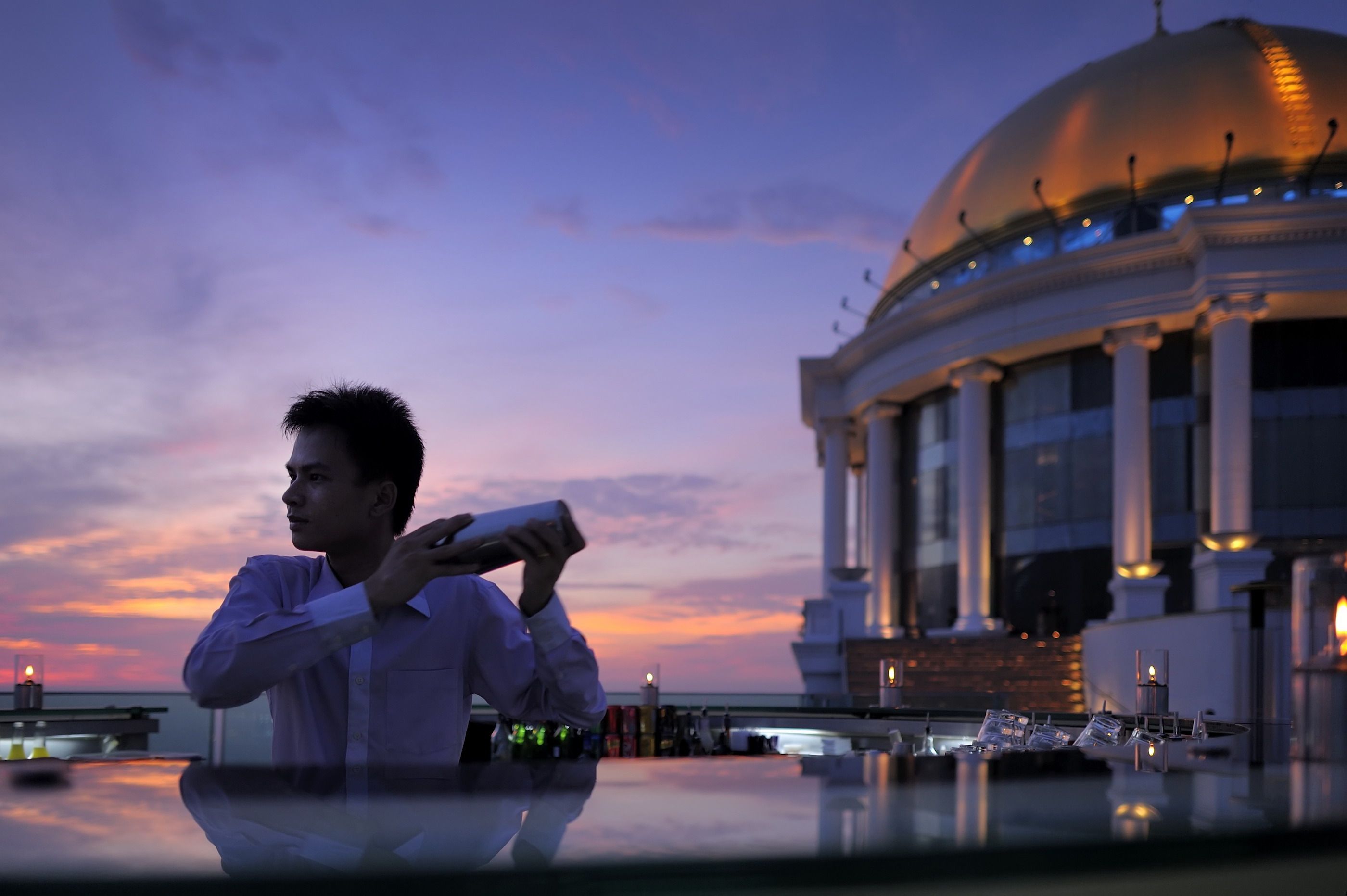 man holding cocktail mixer in bar and yellow dome in background